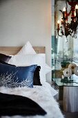 Stack of scatter cushions on bed; partially visible chandelier above bedside table