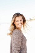 A young woman on a beach wearing a taupe jumper