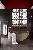 Natural stone bathtub in front of carved Asian-style shutters