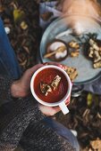 Person hält Tasse mit Tomatencremesuppe in den Händen