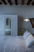 White wardrobe with mirrored panel next to double bed below rustic wood-beamed ceiling