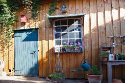 Blue-grey wooden door and flowering geraniums below lattice window in façade of idyllic wooden cabin