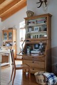 Table lamp on stripped wooden bureau and cane chair in open-plan country-house interior