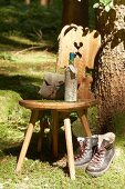 Wooden chair, hiking utensils, wine bottle wrapped in map and walking boots below tree