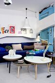 Set of coffee tables in front of royal-blue couch and white wall-mounted shelves in eclectic interior