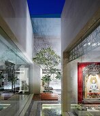 Architectural courtyard of contemporary, Indian house with view of illuminated Hindu shrine through glass wall