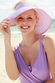 Junge Frau in lila Strandkleid und Sonnenhut steht am Meer