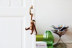 Monkey figurine hanging from handle of sliding door, green glass vase and magazine rack in living area