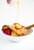 Vanilla sauce being poured over strawberry and polenta slices