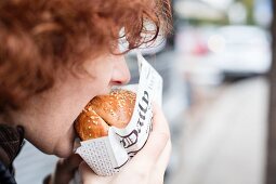 A red-haired teenager biting into a hamburger