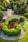 Angelegter Gartenplatz mit rot blühendem Begonienbeet, Buchshecke und Kunstwerk auf Sockel