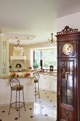 Antique, elegant long-case clock and open-plan, white, country-house kitchen with chandeliers
