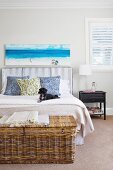 Rattan chest in front of a double bed with a padded headboard and picture with a sea motif