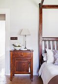 Wooden bedside table with table lamp next to bed with canopy frame
