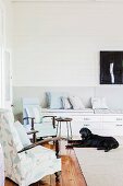 Corner of living room with two armchairs in front of bench with drawers, dog in front of carpet