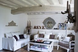 White sofa set with scatter cushions and antique armchair in living room with white wood-beamed ceiling