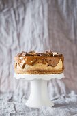 A Snickers cheesecake with caramel ganache on a cake stand