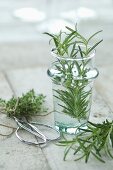 Fresh rosemary in a glass with fresh thyme on a wooden surface in the background