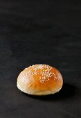 A burger bun with sesame seeds on a dark surface