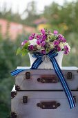 Romantic flower arrangement with blue striped ribbon and elegant brooch on stacked vintage suitcases