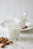 Two glasses of vegan almond milk and scattered almonds