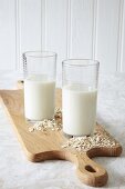 Two glasses of vegan oat milk with oats on a chopping board