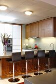 Open-plan, modern kitchen with breakfast bar and elegant, brown leather bar stools; designer ambiance