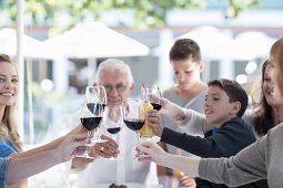 A family eating together at a terrace table: raising a toast with glasses of red wine and lemonade