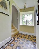 Patterned tiled floor, lattice window and arched doorway over staircase in hallway