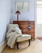 Antique easy chair and chest of drawers in corner of room painted pale blue