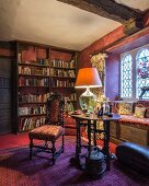 Antique chair and table lamp on table in front of window seat in traditional library