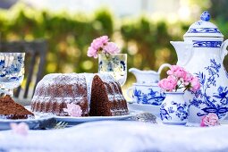 A sliced chocolate Bundt cake on a table laid for coffee in a garden