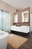 Spacious bathroom with walls painted pale brown, rug in front of washstand and glazed shower area