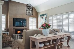 Lounge area, carved wooden console table against back of sofa and flatscreen TV on wall painted light brown