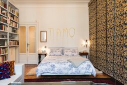 Double bed below lovers' message on wall and next to fabric sliding elements in bedroom