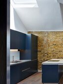 Minimalistische blaue Designerküche mit Ziegelwand unter Dachflächenfenster im renovierten Dachgeschoss