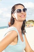 Brünette Frau mit feuchtem Haar und Sonnenbrille am Strand