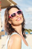 A brunette woman on a beach with damp hair and sunglasses