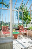 Rote Gartenstühle und Tischchen aus Terrakottatopf im Gewächshaus mit Kiesboden