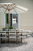 Seating area below parasol on gravel terrace outside wooden house