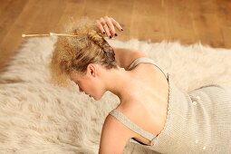 A woman wearing a knitted dress fixing her hair with knitting needles