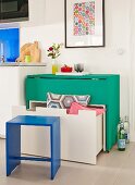 Eingeklappter, rollbarer, grüner Tisch mit untergeschobener weißer Sitzbank und Schublade; Stauraumlösungen mit platzsparendem Mobiliar