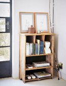 Books and framed pictures on vintage wooden shelves next to fishing rod leant against wall in corner