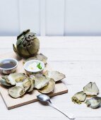 Cooked artichokes on a wooden board with aioli and vinaigrette