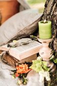 Romantischer Platz mit Kerze und Blüten neben aufgeschlagenem Buch an Baumstamm