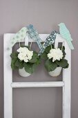 Bird ornaments hand-crafted from coloured paper and corrugated cardboard decorating potted white primulas hung on vintage window frame