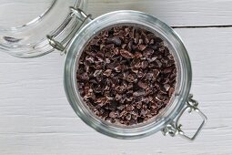 Cocoa nibs in a flip-top jar on a white wooden surface