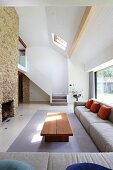 Exotic-wood coffee table and pale grey corner sofa in open-plan, high-ceilinged interior with staircase in background