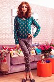 A young woman wearing a polka-dot jumper and trousers standing in front of an upholstered sofa