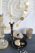 Gold bemalte Steine in schwarzer Backform und Kerzenhalter mit weissen Kerzen weihnachtlich geschmückt, vor Girlande aus goldenen Papierplättchen